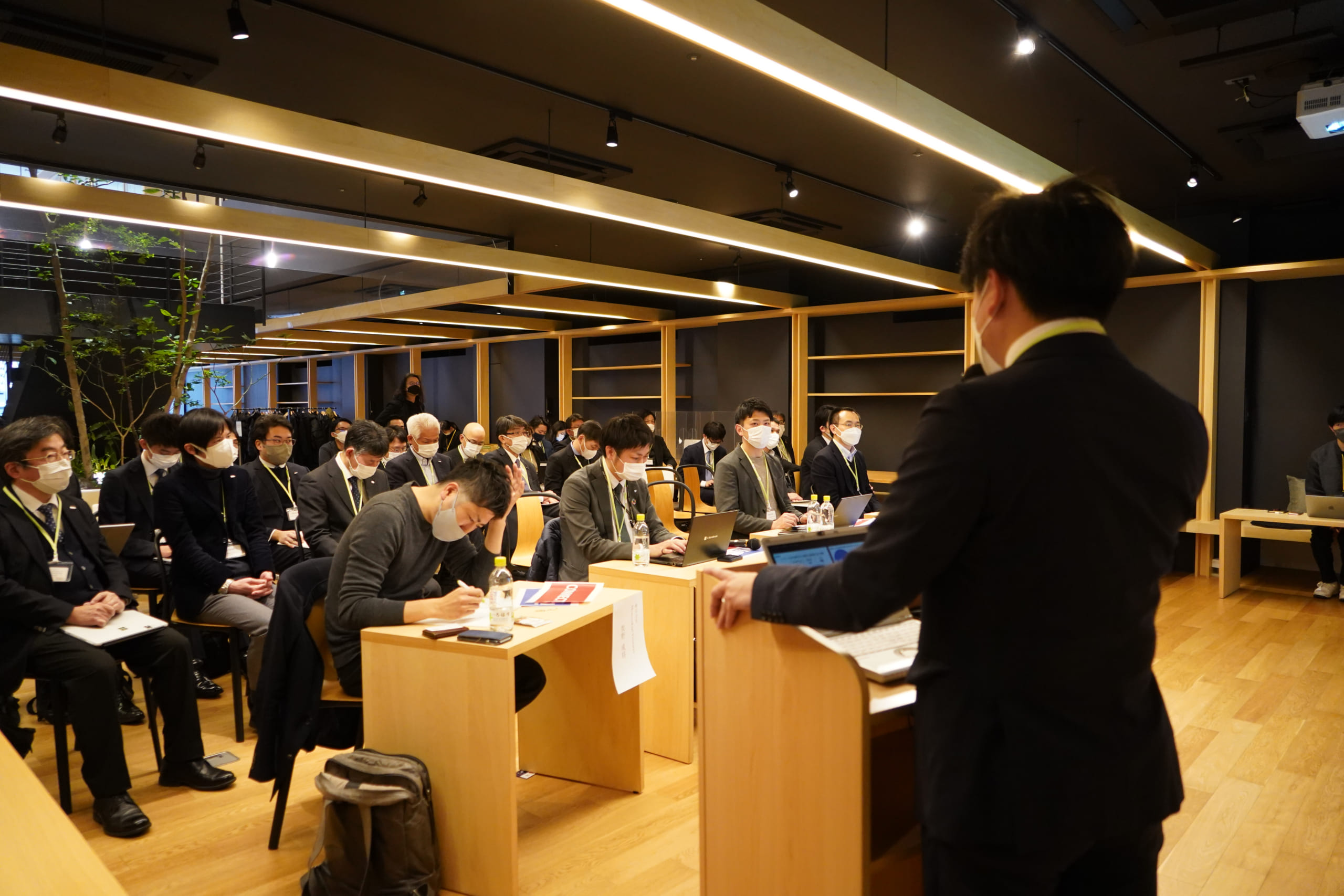 A presenter is speaking from a speaker podium and VCs sitting in the front row are taking notes.